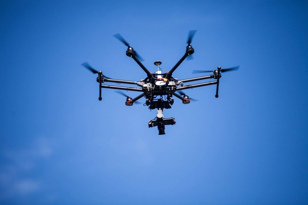 Multikopter-Drohne mit Kameragimbal im Steigflug vor blauem Himmel